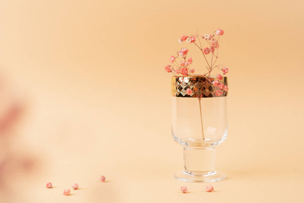 Beautiful glass goblet with golden rims and flowers inside on nude cream fabric - Foto, afbeelding