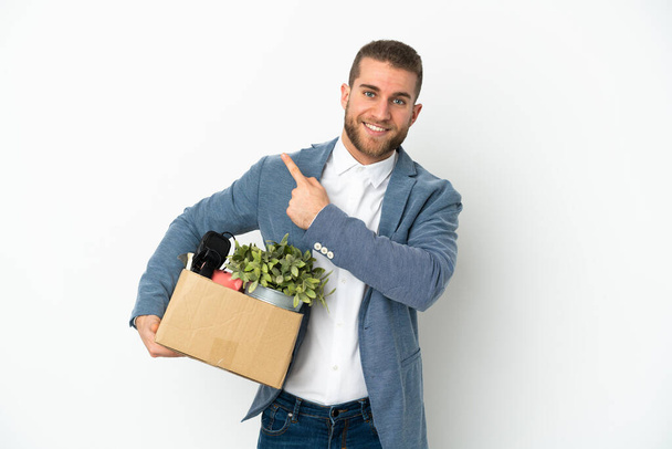 Young caucasian making a move while picking up a box full of things isolated on white background pointing to the side to present a product - Fotografie, Obrázek