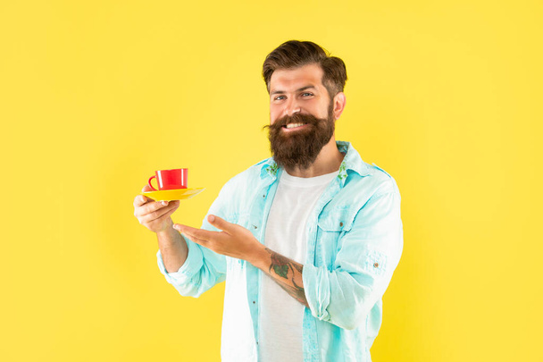 glad unshaven man in shirt showing coffee on yellow backdrop, beverage - Valokuva, kuva