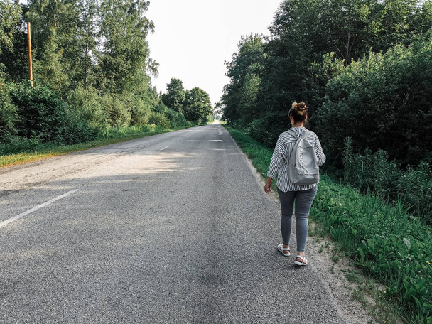 a female tourist with a backpack walks along an asphalt road in the countryside. - Photo, image