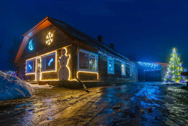 Paisagem noturna com um quintal decorado de Natal, decorações leves, reflexos de luz coloridos em uma estrada molhada em primeiro plano - Foto, Imagem
