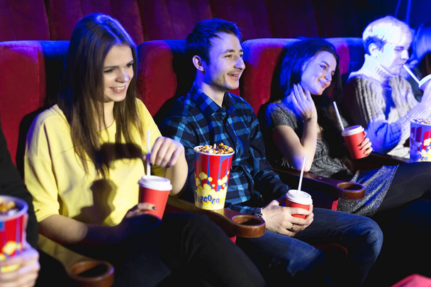 Friends sit and eat popcorn together while watching movies in a movie theater. - Fotoğraf, Görsel