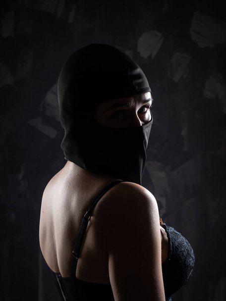 Portrait d'une fille en cagoule noire et soutien-gorge noir. Tourné en studio sur un fond sombre. - Photo, image