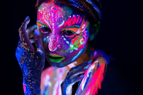 Fashion model woman in neon light, portrait of beautiful model girl with fluorescent make-up, Body Art design of female disco dancer posing in UV, painted face, colorful make up, over black background - Foto, imagen