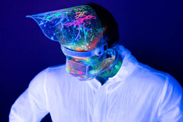 Portrait of man doctor in protective clothes in ultraviolet neon light during coronavirus pandemic. Epidemic, pandemic of coronavirus covid-19. - Fotografie, Obrázek