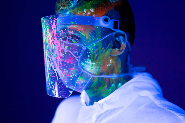Portrait of man doctor in protective clothes in ultraviolet neon light during coronavirus pandemic. Epidemic, pandemic of coronavirus covid-19. - Fotografie, Obrázek