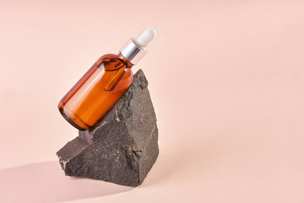 Essential oil on a granite stone on a beige background. Cosmetic medical beauty product in brown glass bottle with a pipette for aromatherapy, alternative medicine. - Foto, afbeelding