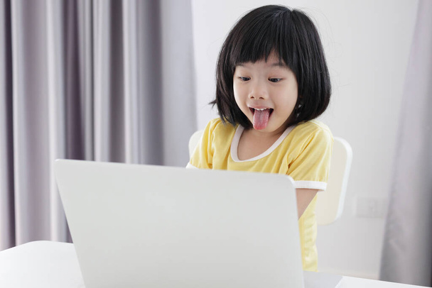 小さなアジアの女子学生は自宅のノートパソコンを使ってオンラインで勉強し - 写真・画像