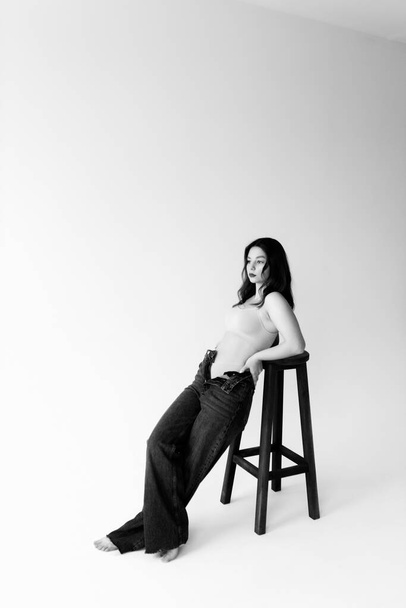 Joven modelo sexy posando para la foto con taburete de bar en el estudio sobre fondo blanco.  - Foto, imagen