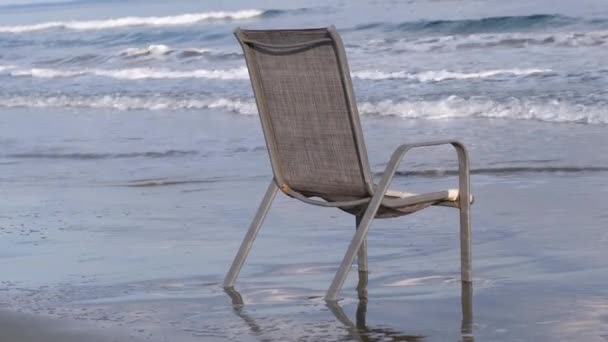 Woestijnstoel gelegen aan een verlaten strand wordt bereikt door ruwe zee golven- winter scene strand concept op McKenzie strand in Larnaca - Video