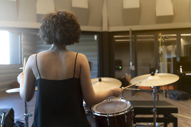 Νεαρή γυναίκα με σγουρά μαλλιά παίζει ντραμς σε στούντιο ηχογράφησης - Φωτογραφία, εικόνα