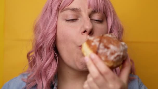 Viehättävä nuori ihana naaras puree makea donitsi eristetty keltaisella taustalla - Materiaali, video