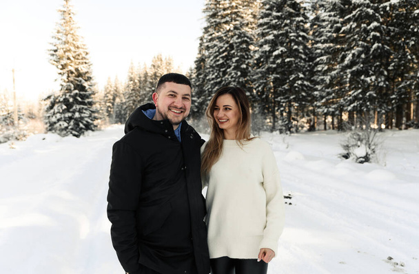 Young couple on the snow in winter in the park. love and vacation concept - happy couple hugging and laughing outdoors in winter - Fotó, kép