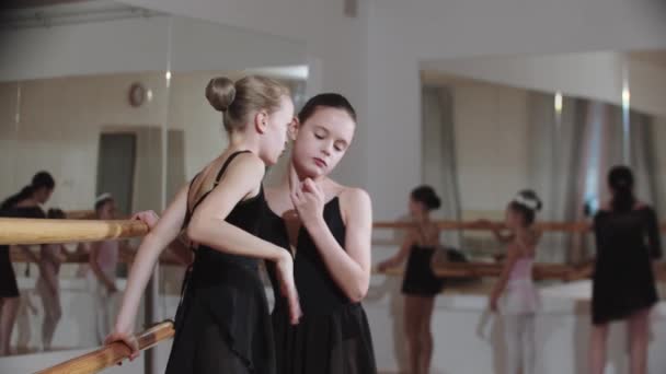 Две маленькие девочки шепчут что-то друг другу возле стенда балетной студии - Кадры, видео