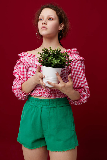 привлекательная молодая женщина в розовой блузке позирует с растением в белом горшке - Фото, изображение