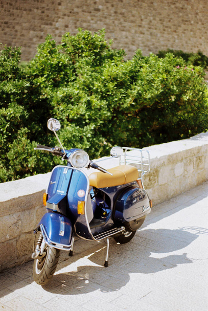 Mavi motosiklet taş bir çitin yanındaki kaldırım taşlarının üzerinde duruyor. - Fotoğraf, Görsel
