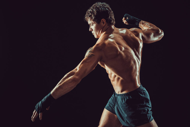 Side view of muscular shirtless boxer who strikes isolated on dark background. Sport concept - Foto, Bild