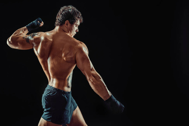 Side view of athlete shirtless boxer who strikes isolated on dark background. Sport concept - Фото, зображення