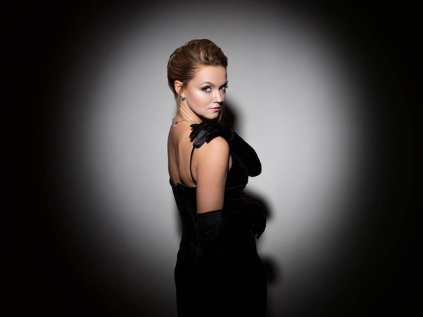 A femme fatale in a black dress with an open back and long velvet gloves. - Photo, Image
