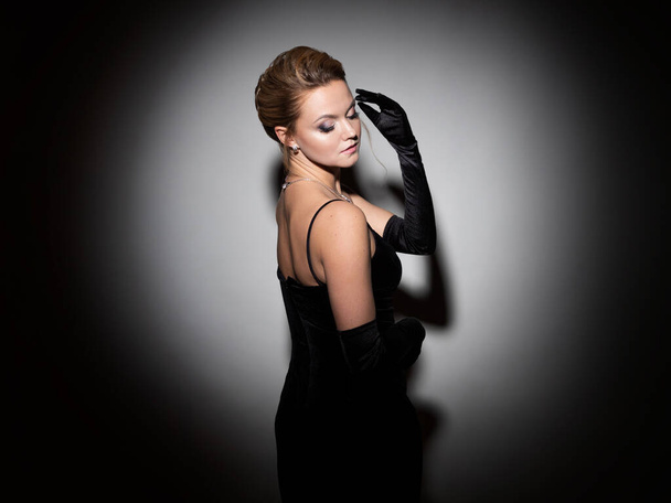 A femme fatale in a black dress with an open back and long velvet gloves. - Photo, image