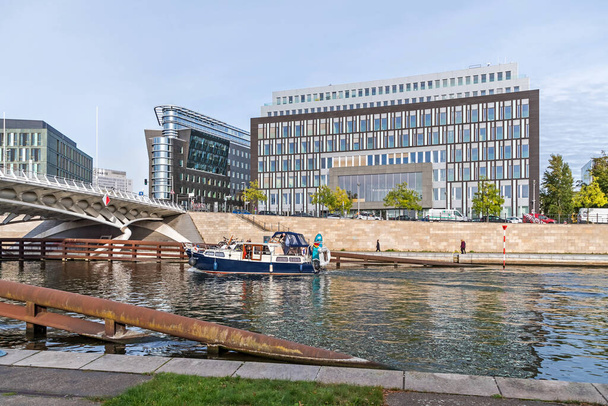 Berlín, Německo - 18. října 2021: Břehy řeky Sprévy Kapelle Ufer s budovami SoftEd Systems s reflektující fasádou a tiskovou konferenční budovou, mostem korunního prince a rekreační lodí - Fotografie, Obrázek