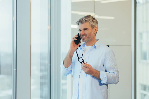Businessman talking on the phone, gray-haired and experienced man looking at camera and smiling, man at work - Foto, immagini