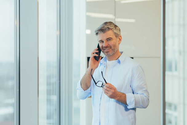 Businessman talking on the phone, gray-haired and experienced man looking at camera and smiling, man at work - Foto, Imagen