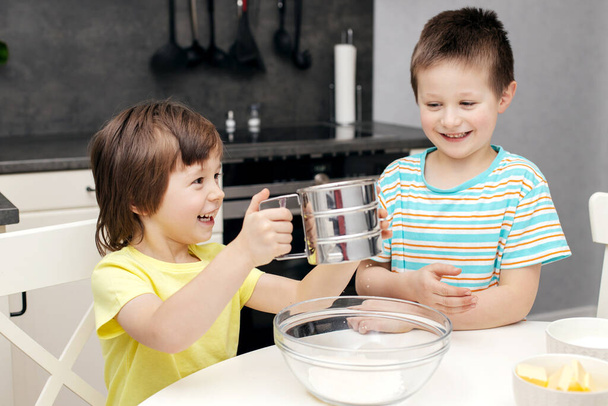 A gyerekek tésztát készítenek a konyhában. A fiúk otthon főznek. Otthon a gyerekekkel. Kis szakácsok - Fotó, kép