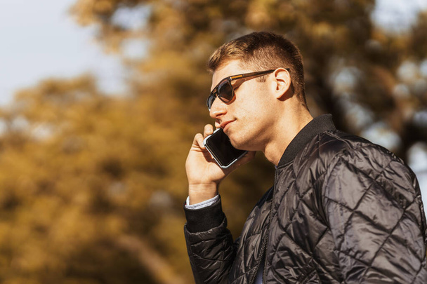 Ein Mann mit Sonnenbrille hört eine Audiobotschaft auf seinem Handy. - Foto, Bild