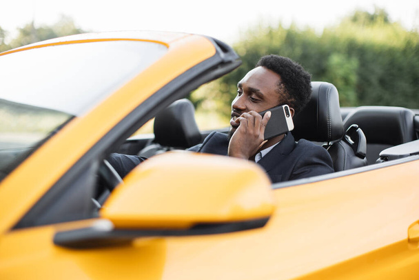 Handsome African businessman talking on the mobile phone while sitting on back seat of a sport car. - Fotoğraf, Görsel
