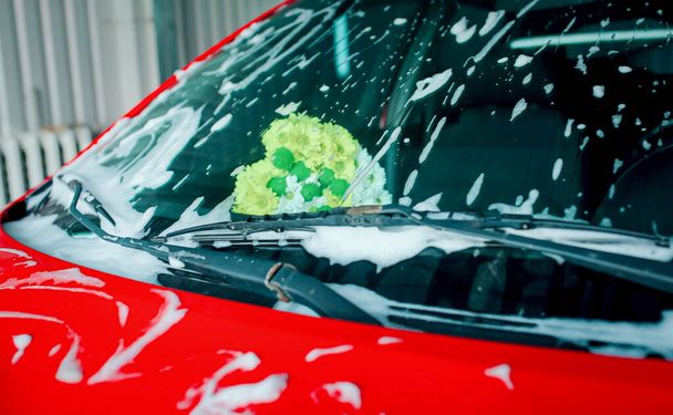 Bouquet of flowers in the car behind the windshield. Washing car. Driver's glass in foam. - Foto, Bild