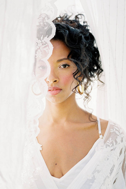 Retrato de una mujer con un vestido blanco asomándose detrás de una cortina - Foto, Imagen