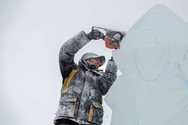 De beeldhouwer snijdt ijs contouren van ijs met een kettingzaag voor Kerstmis - Foto, afbeelding