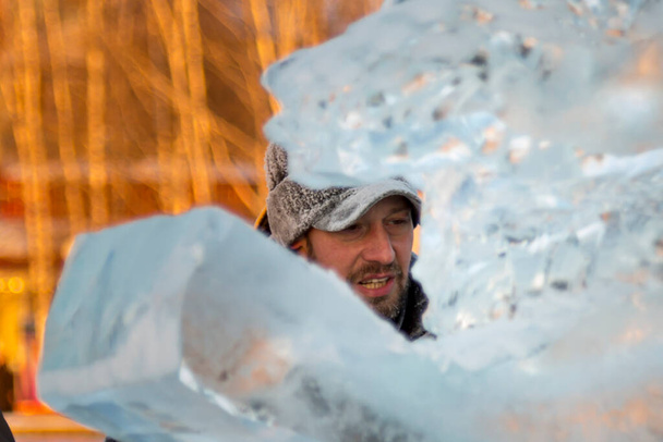 Porträt eines arbeitenden Monteurs in Winterjacke und schwarzer Mütze mit Visier in der Nähe des Eises - Foto, Bild