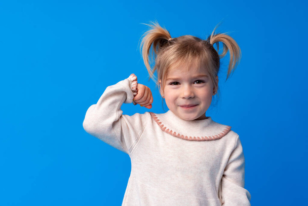 Little cute girl showing her strength against blue background - Foto, afbeelding