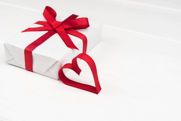 バレンタインデーやコピースペース付きの誕生日のコンセプト。白い木の赤いリボンハートとギフトボックス - 写真・画像