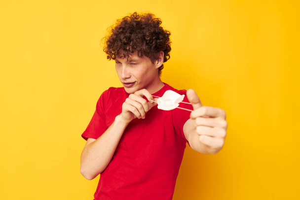 portrait of a young curly man in a red t-shirt medical mask protection yellow background unaltered - Valokuva, kuva