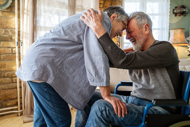 Glückliches Senioren-Liebespaar. Reifer Mann mit Behinderung im Rollstuhl verbringt Zeit mit seiner Frau zu Hause - Foto, Bild