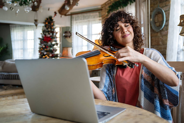 Woman music teacher talking with a student and giving instructions, teaching how to play a song the violin online during a video call - Photo, Image