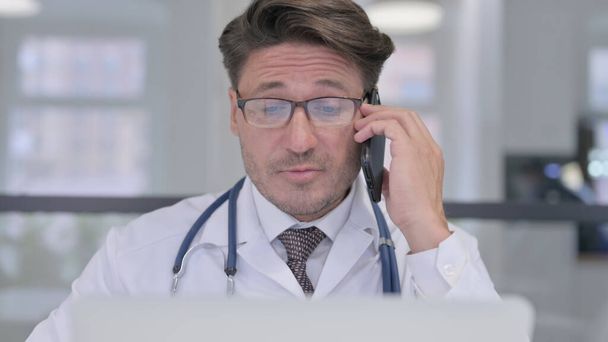 Primo piano del medico con il computer portatile che parla sul telefono - Foto, immagini