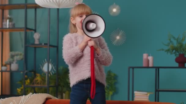 Bambino ragazza bambino in piedi sul divano a casa da solo urlare ad alta voce in megafono annuncia sconti vendita - Filmati, video