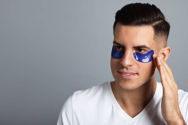 Man applying blue under eye patch on grey background. Space for text - Foto, Bild