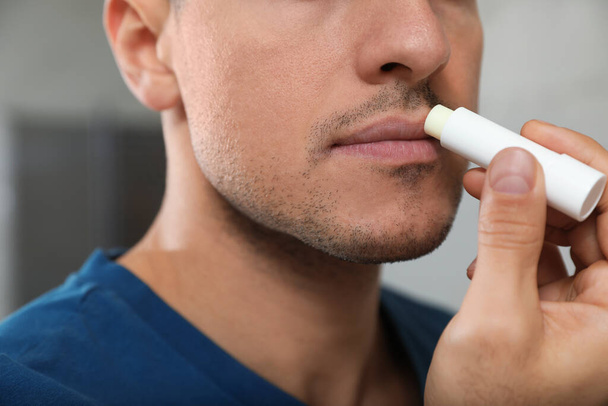 Man applying hygienic lip balm indoors, closeup - Фото, изображение