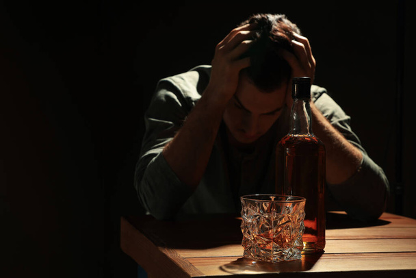 Addicted man and alcoholic drink at wooden table against black background, focus on glass - Photo, Image