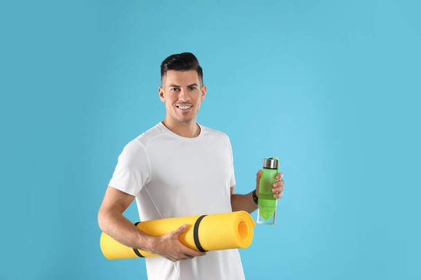 Handsome man with yoga mat and bottle on turquoise background - Fotó, kép