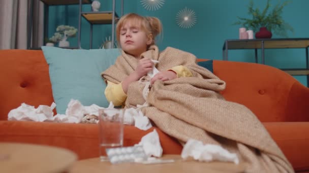 Kind meisje in plaid lijden aan Coronavirus of allergie, niest snot in servet op de bank thuis - Video