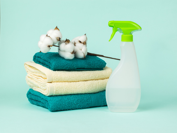A linen care product, a set of towels and a sprig of cotton on a blue background. The concept of laundry and laundry care. - Photo, Image