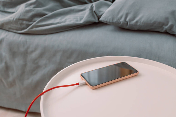 携帯電話は自宅の寝室のベッドの近くのコーヒーテーブルのバッテリーを充電します. - 写真・画像