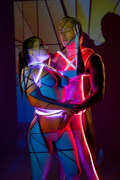 Naked couple with neon ropes embracing against colorful background - Foto, immagini