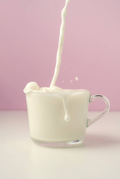 Milk is poured into a transparent cup on a purple background. - Zdjęcie, obraz